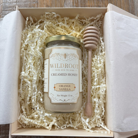Jar of Wildroot creamed honey with a honey dipper in a gift box on a wooden surface
