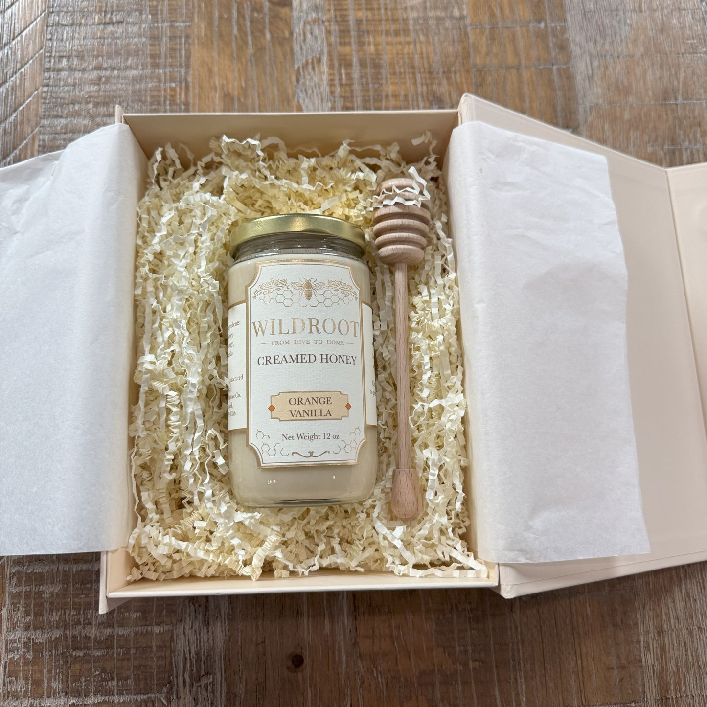Jar of creamed honey with a honey dipper in a gift box on a wooden surface